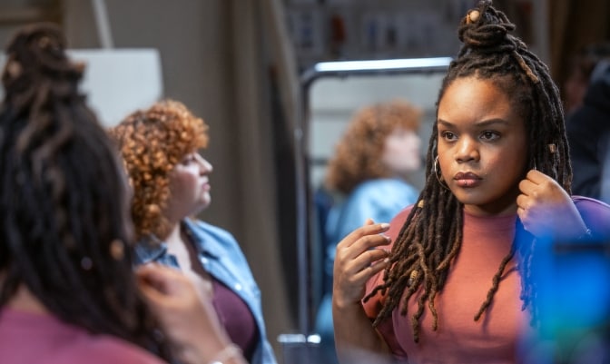 Woman looking in a mirror and touching her hair with another woman in the background